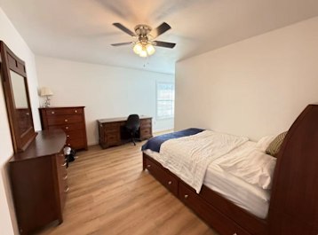 Private furnished bedroom with queen bed, desk, and dresser